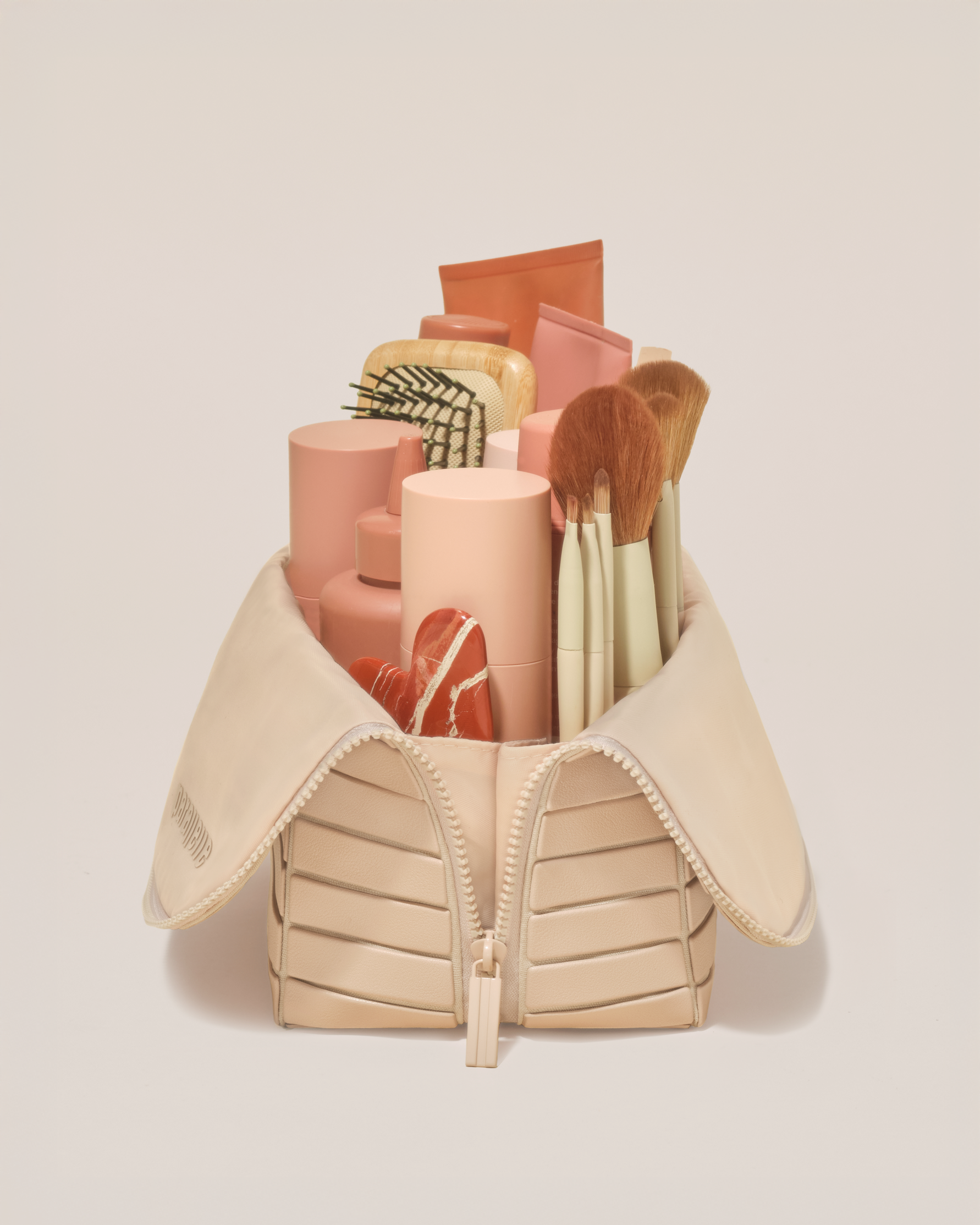 Side profile of the Large Bisque (white) Traveller makeup bag filled with beauty essentials standing upright, showing flexible compartment design