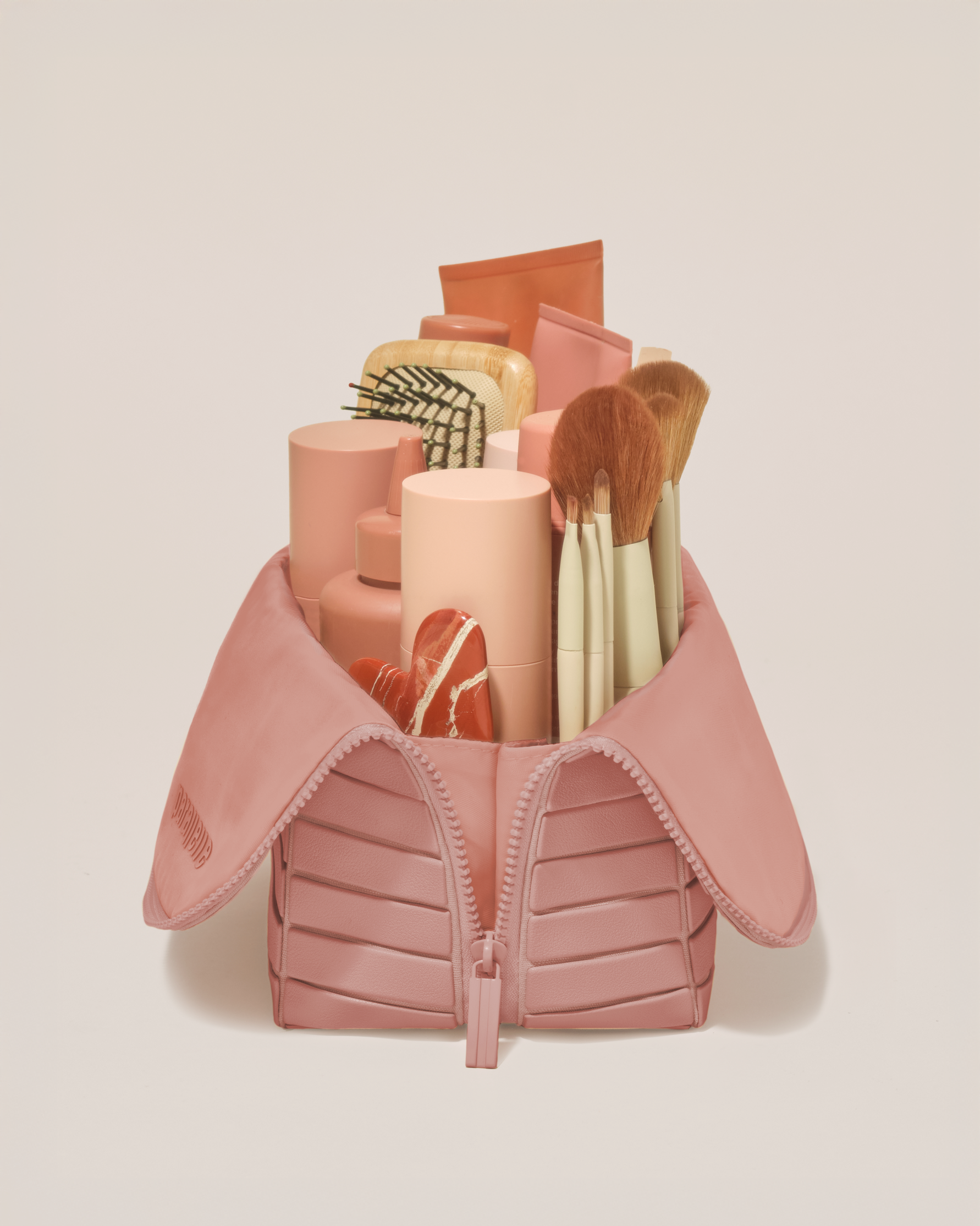 Side profile of the Large Blush (pink) Traveller makeup bag filled with beauty essentials standing upright, showing flexible compartment design