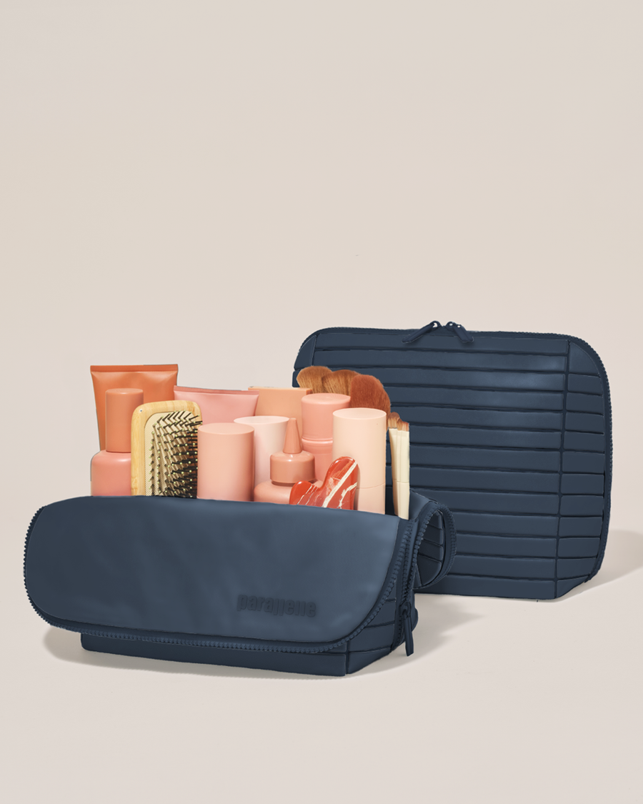 Open and closed Parallelle Large Indigo (navy) Traveller makeup bag showing skincare, brushes, and curated travel essentials
