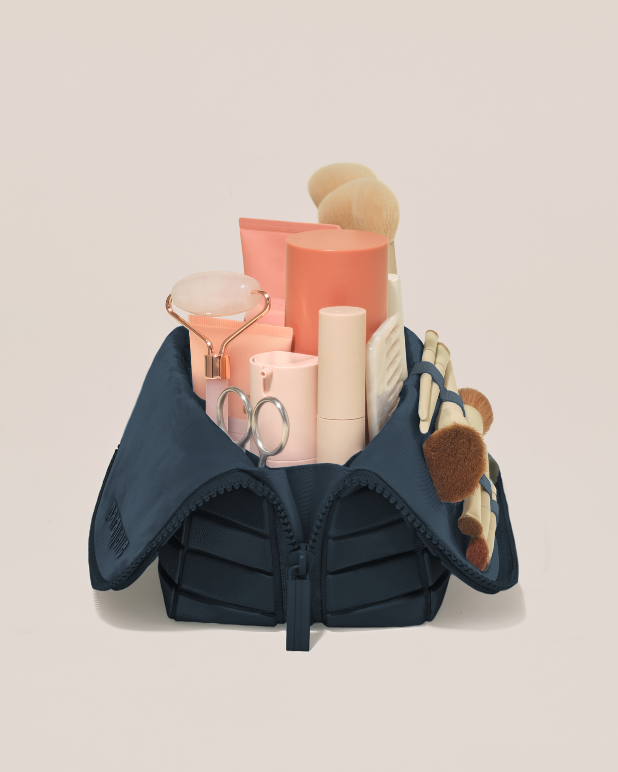 Side profile of the Medium Indigo (navy) Traveller makeup bag filled with beauty essentials standing upright, showing flexible compartment design