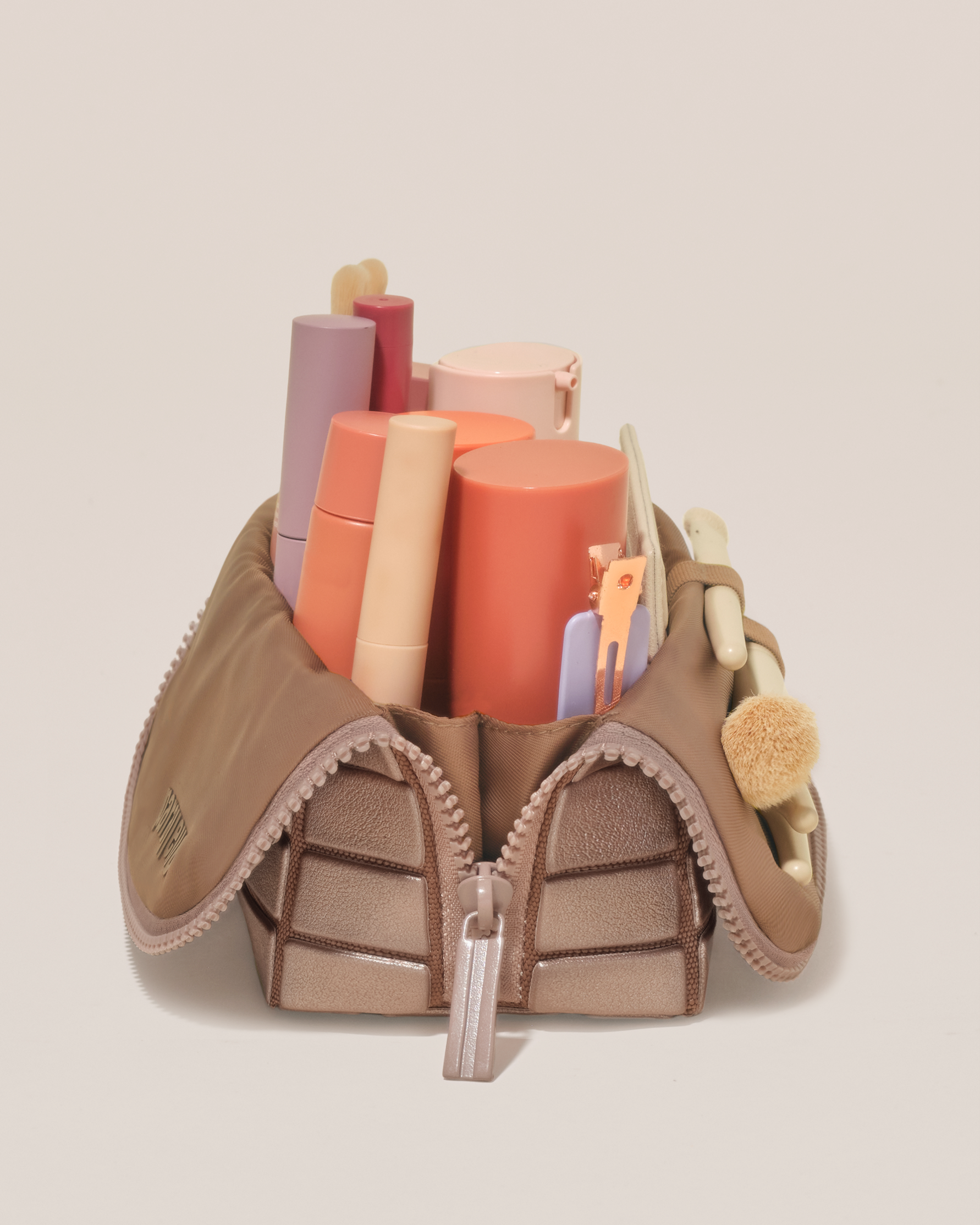 Side profile of the Small Bronze Traveller makeup bag filled with beauty essentials standing upright, showing flexible compartment design