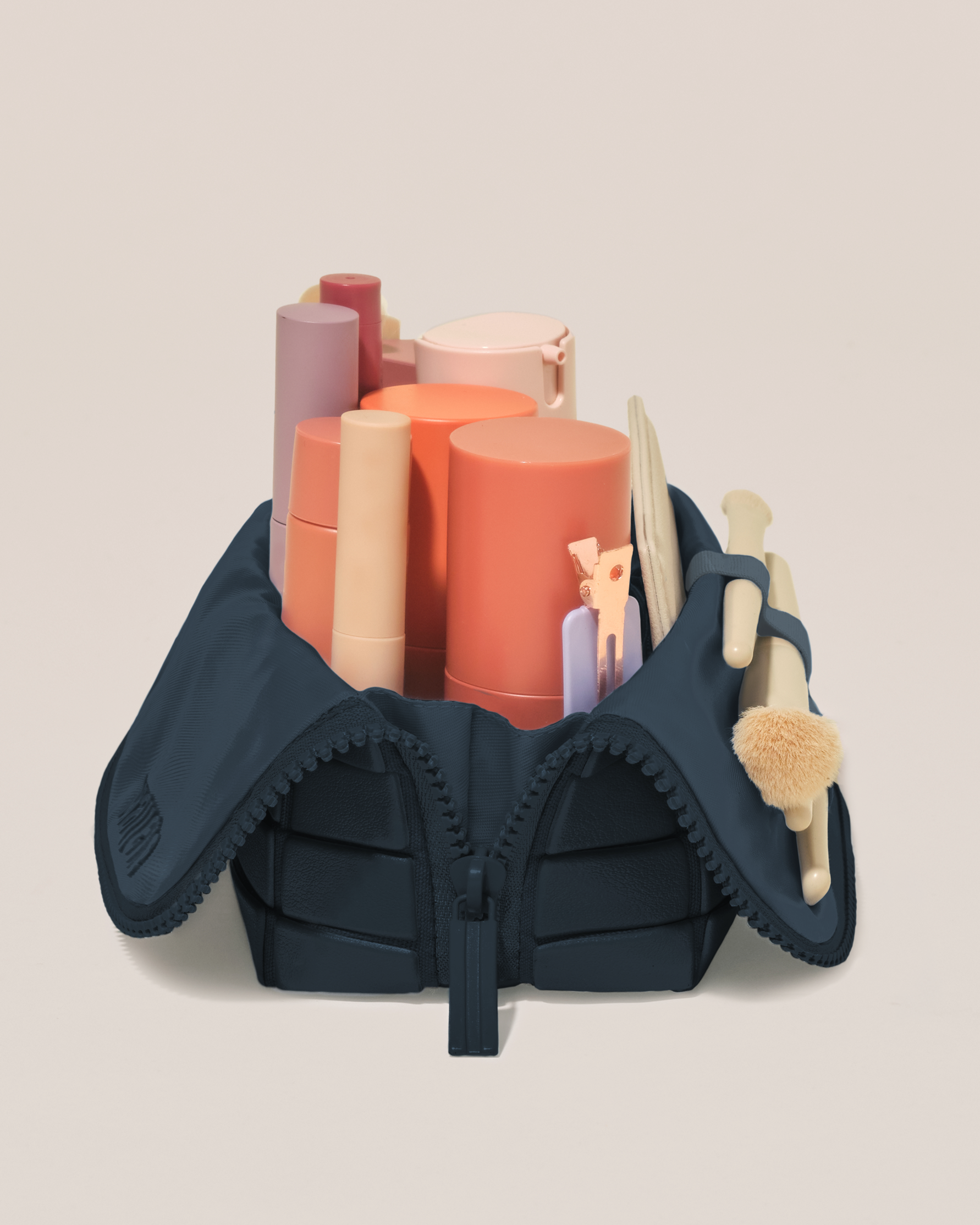 Side profile of the Small Indigo (navy) Traveller makeup bag filled with beauty essentials standing upright, showing flexible compartment design