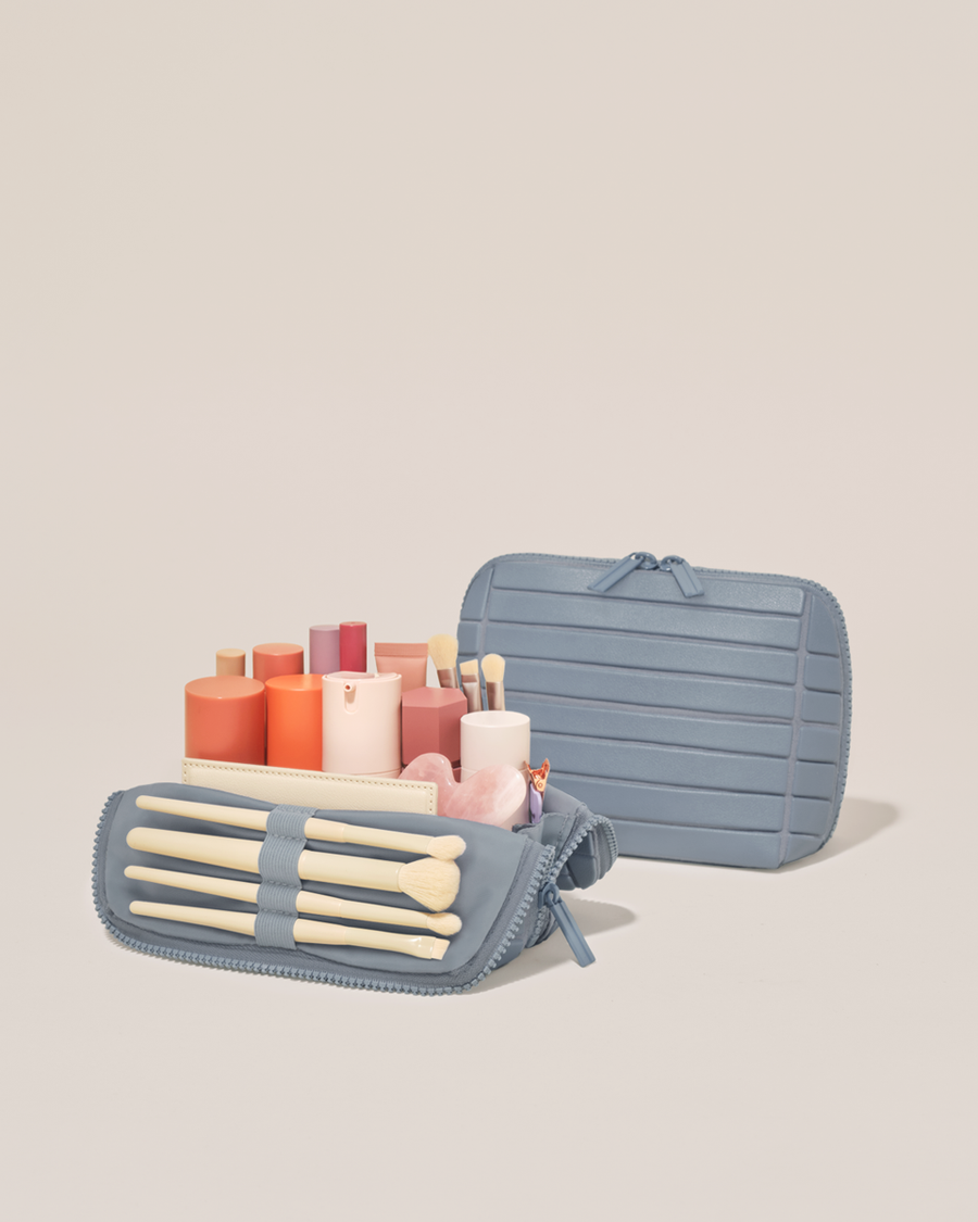 Open and closed Parallelle Small Slate (blue) Traveller makeup bag showing skincare, brushes, and curated travel essentials