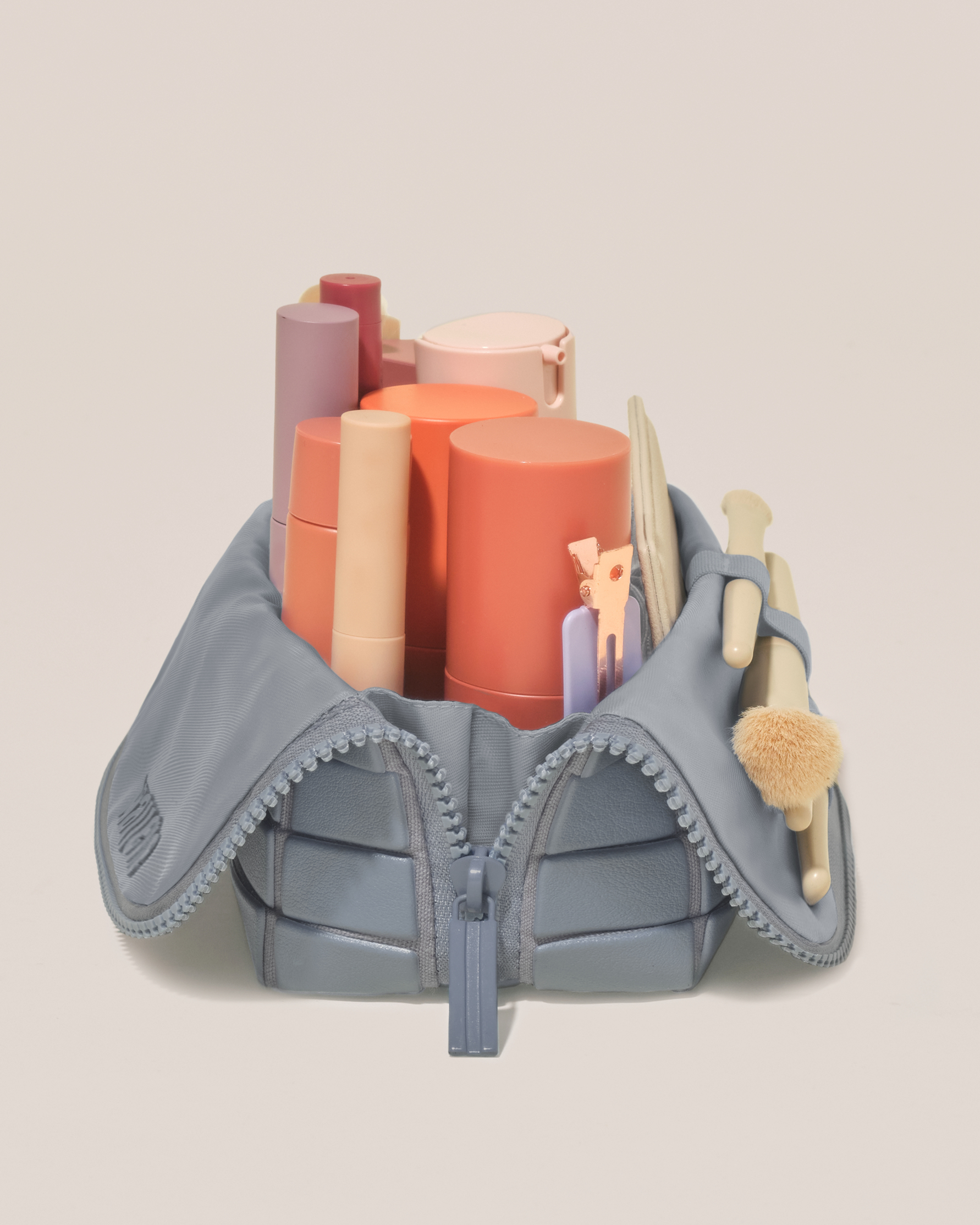 Side profile of the Small Slate (blue) Traveller makeup bag filled with beauty essentials standing upright, showing flexible compartment design