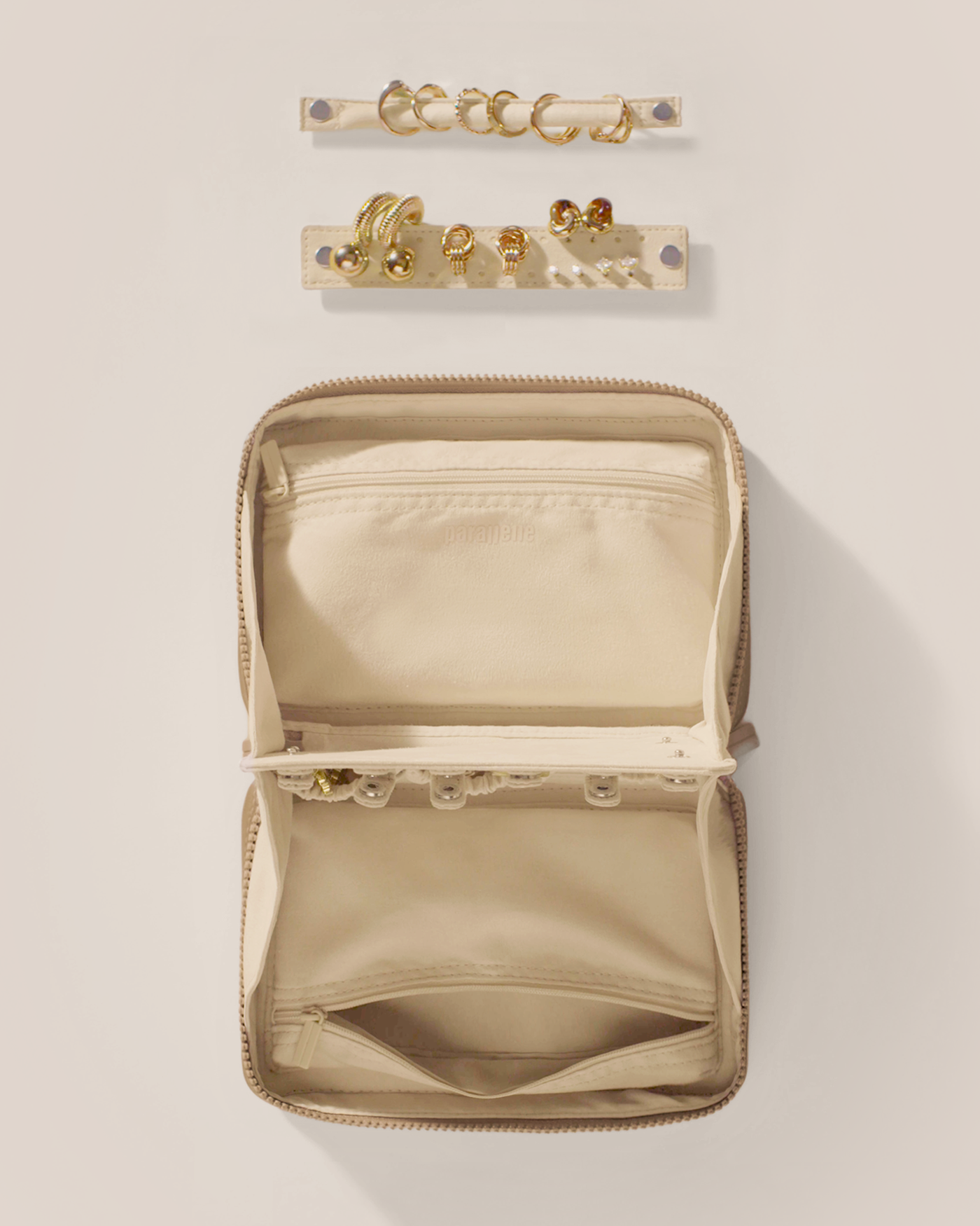 Overhead view of the Parallelle Bronze Vault, showcasing its two-sided interior with one side for rings and earrings and the other for necklaces. Both sides have a zipper pocket for watches and bracelets. The ring and earring bars' removable feature is shown