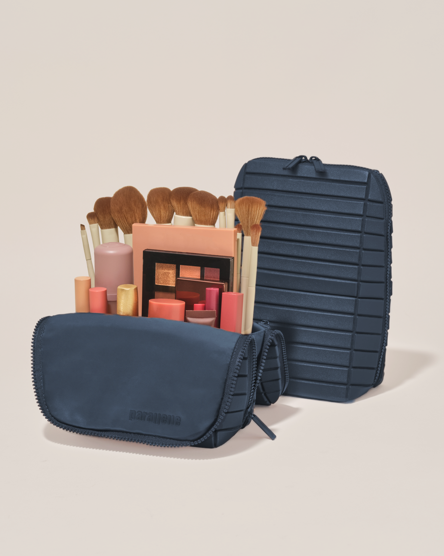 Open and closed Parallelle Indigo (navy) Brush Traveller makeup bag showing skincare, brushes, and curated travel essentials