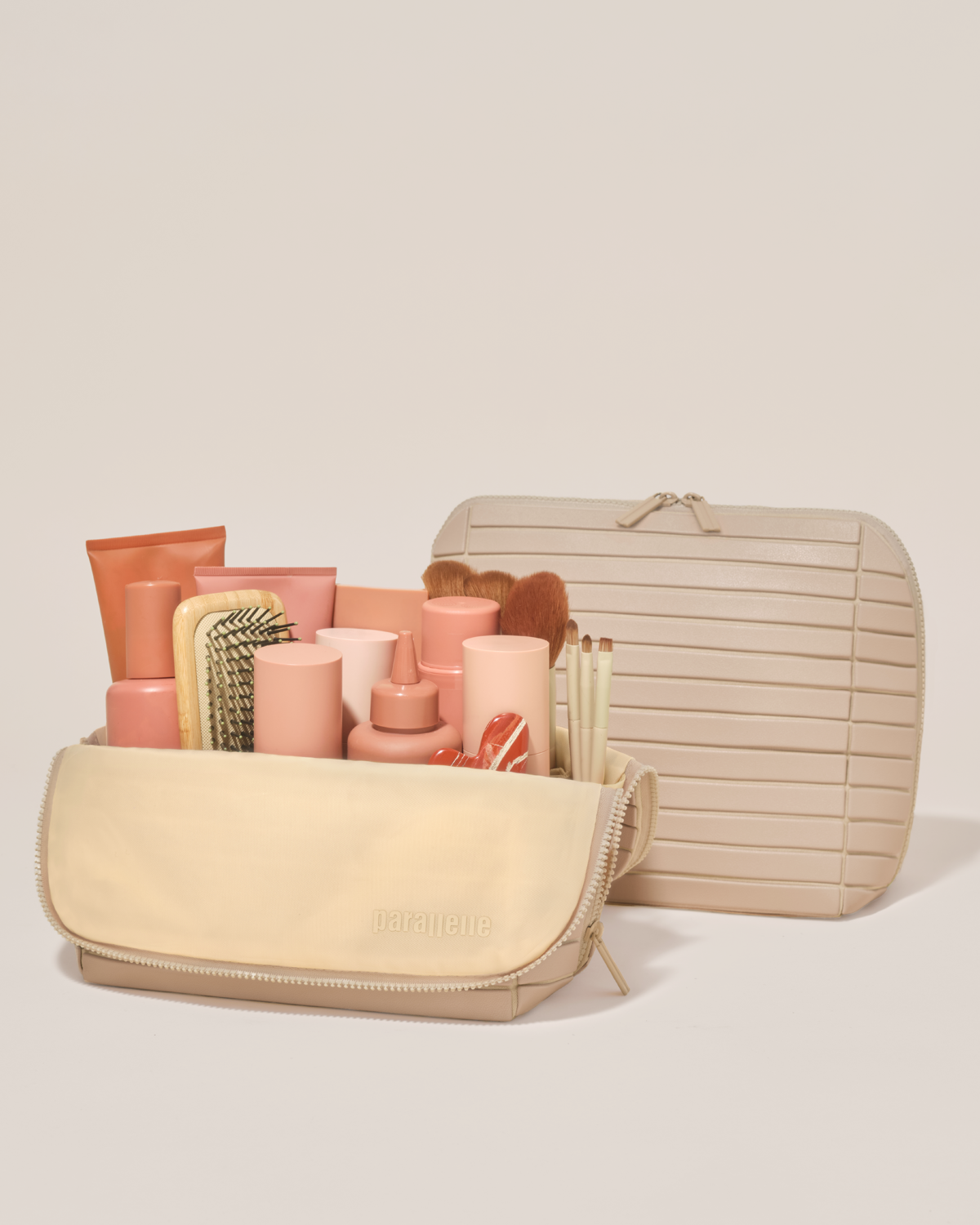 Open and closed Parallelle Large Bisque (white) Traveller makeup bag showing skincare, brushes, and curated travel essentials