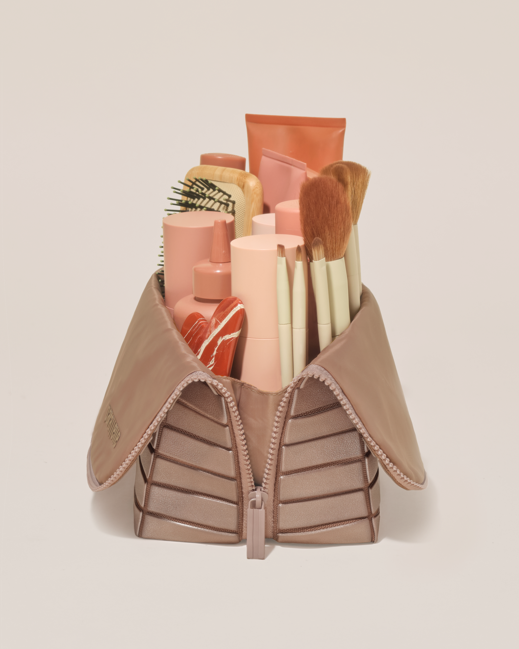 Side profile of the Large Bronze Traveller makeup bag filled with beauty essentials standing upright, showing flexible compartment design