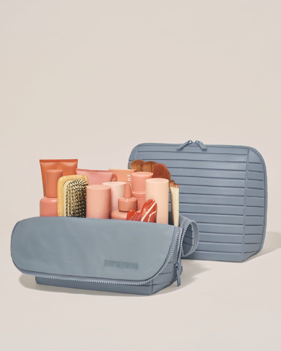 Open and closed Parallelle Large Slate (blue) Traveller makeup bag showing skincare, brushes, and curated travel essentials