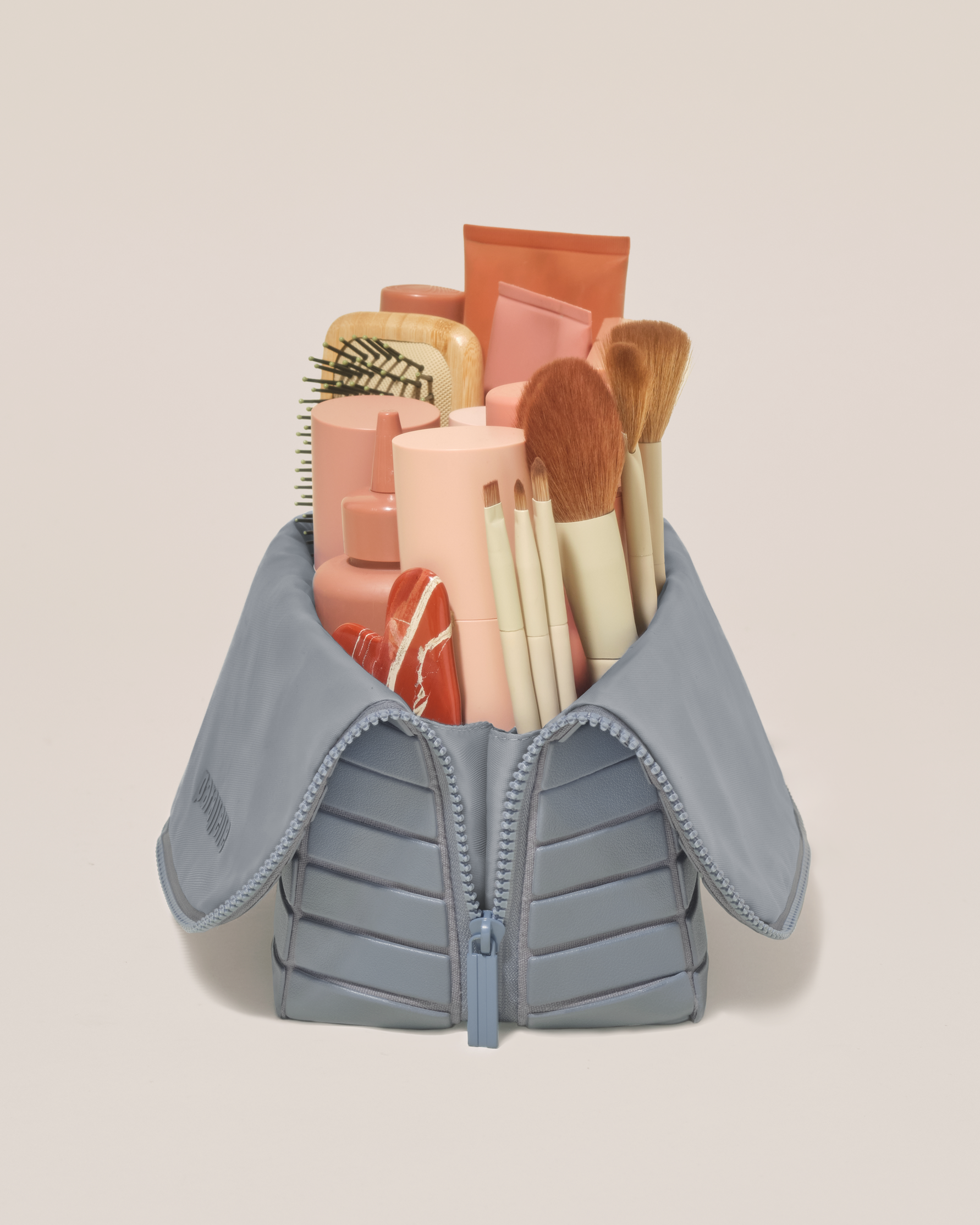 Side profile of the Large Slate (blue) Traveller makeup bag filled with beauty essentials standing upright, showing flexible compartment design