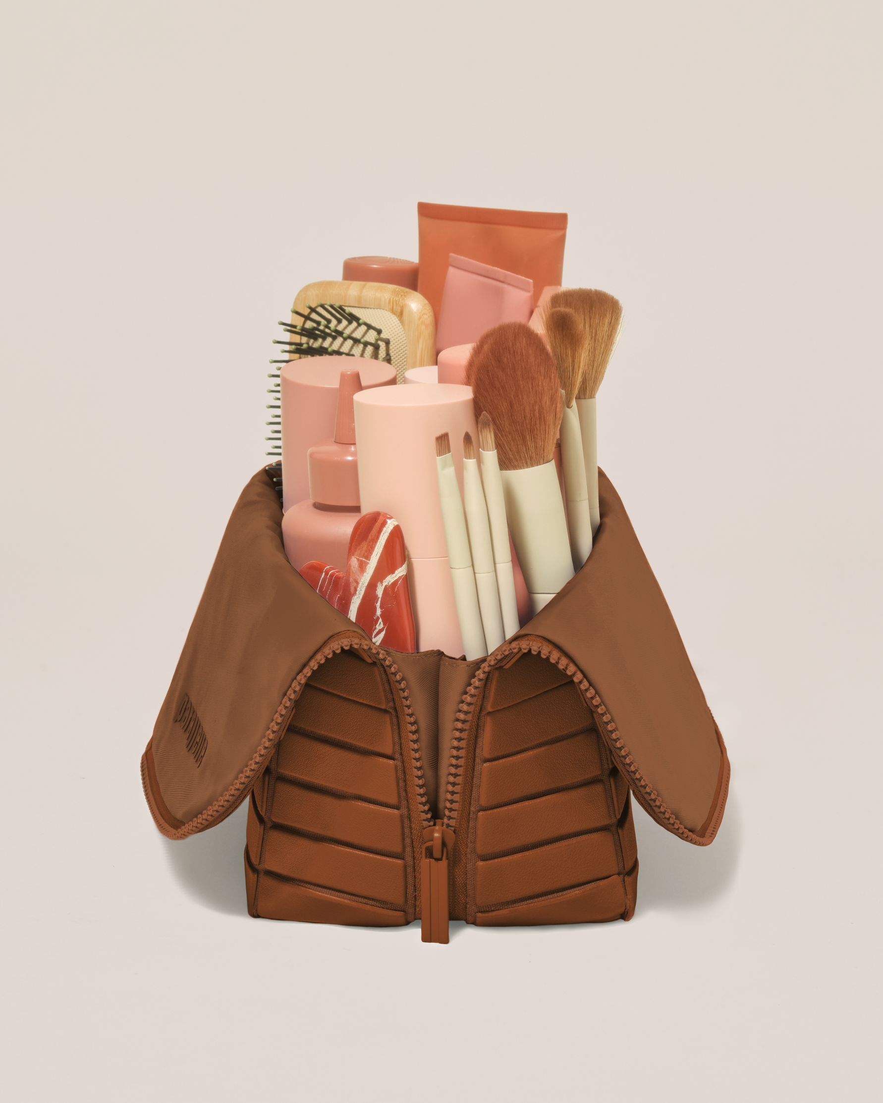 Side profile of the Large Vicuna (brown) Traveller makeup bag filled with beauty essentials standing upright, showing flexible compartment design