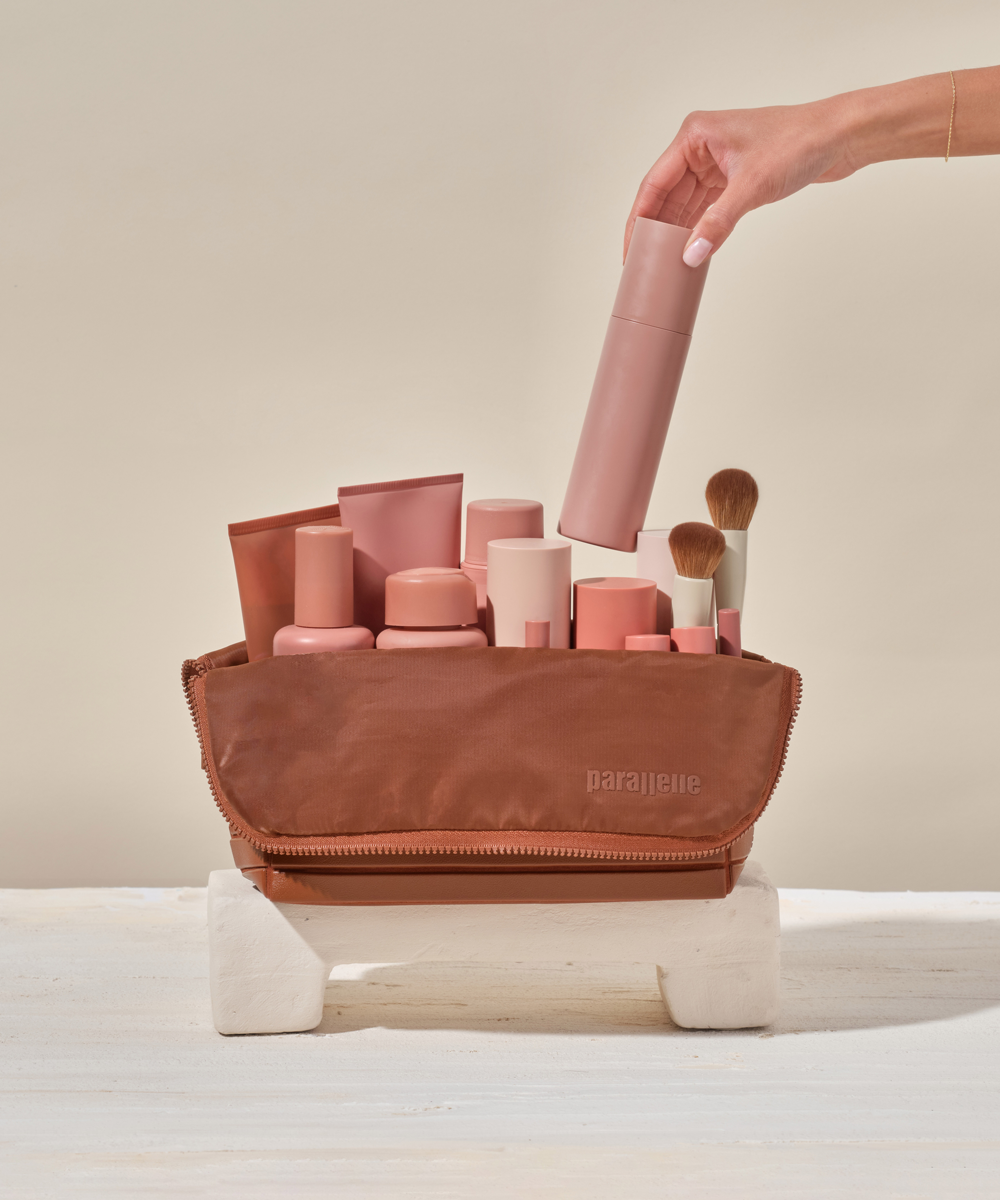 The Large Vicuna Traveller, filled with everyday essentials and beauty products, with a hand placing a bottle inside.