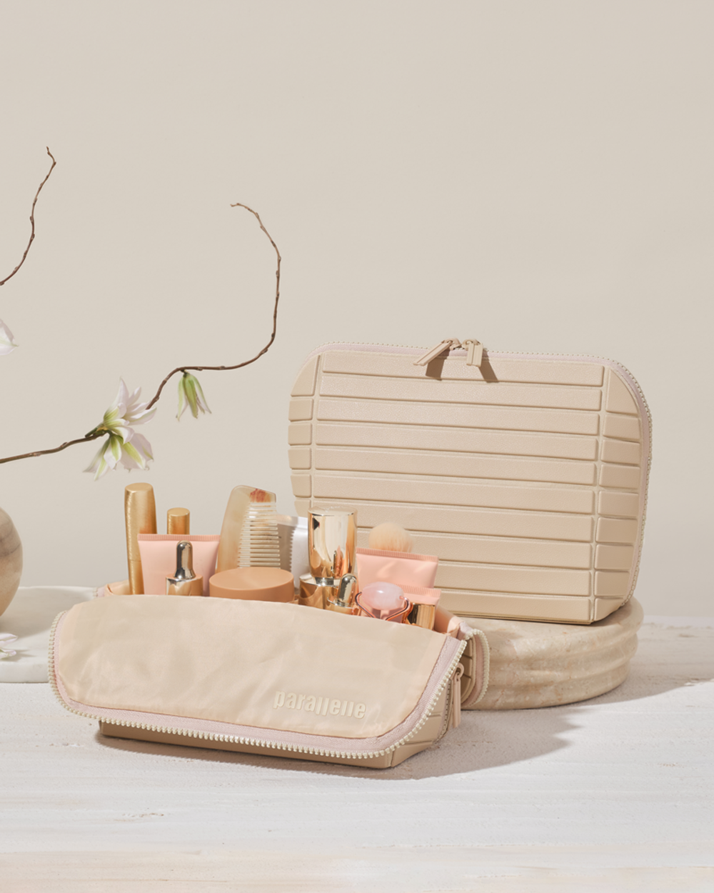 The Medium Bisque Traveller bag, styled with makeup brushes, bottles, and skincare essentials on a light wood surface.
