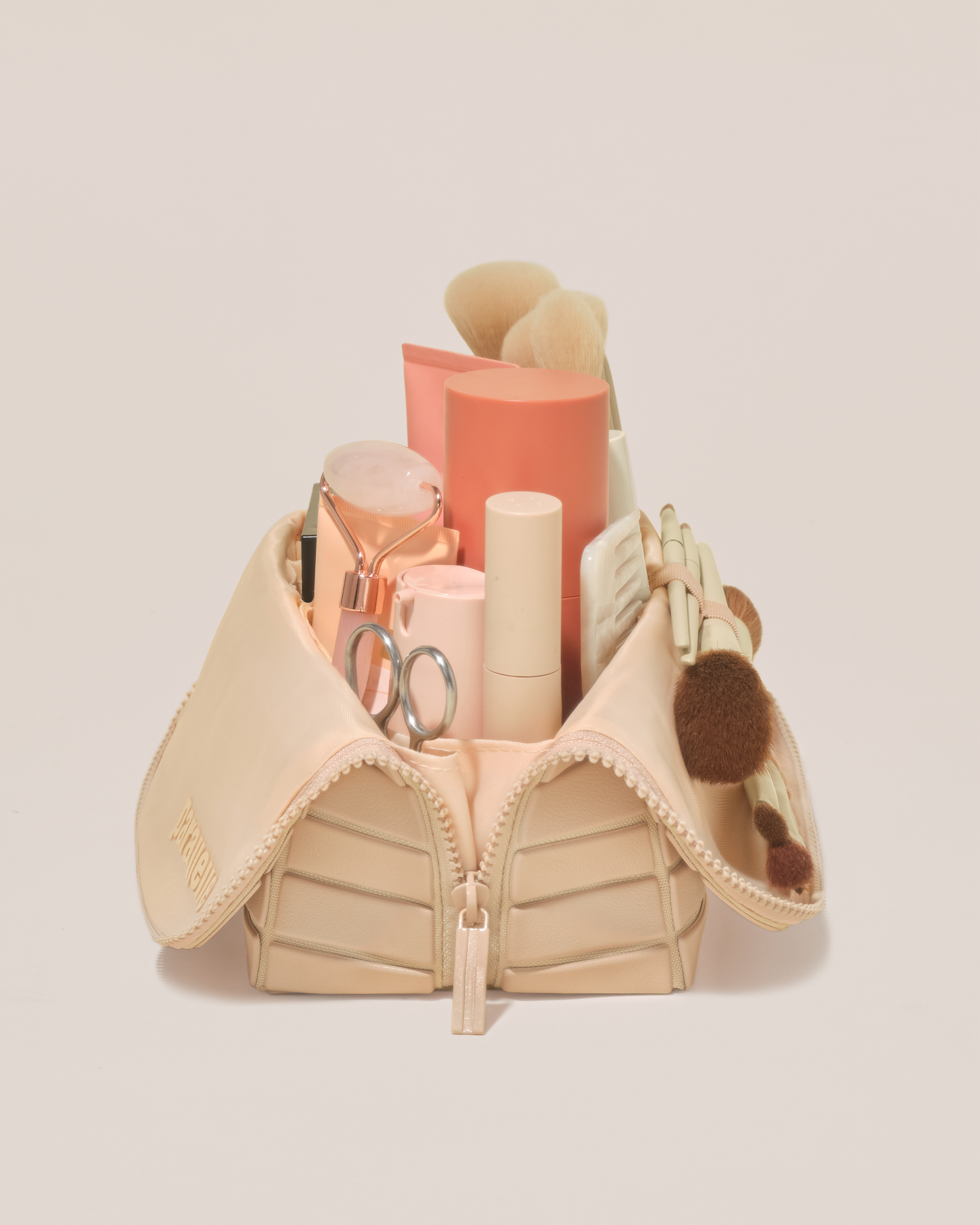 Side profile of the Medium Bisque (white) Traveller makeup bag filled with beauty essentials standing upright, showing flexible compartment design