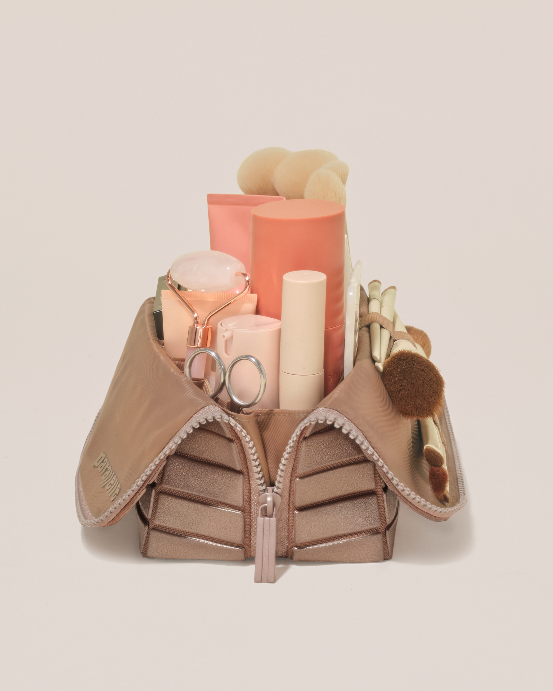 Side profile of the Medium Bronze Traveller makeup bag filled with beauty essentials standing upright, showing flexible compartment design