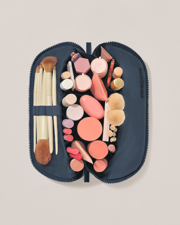 Overhead view of the Medium Indigo (navy) Traveller makeup bag fully packed with upright beauty products and organized compartments