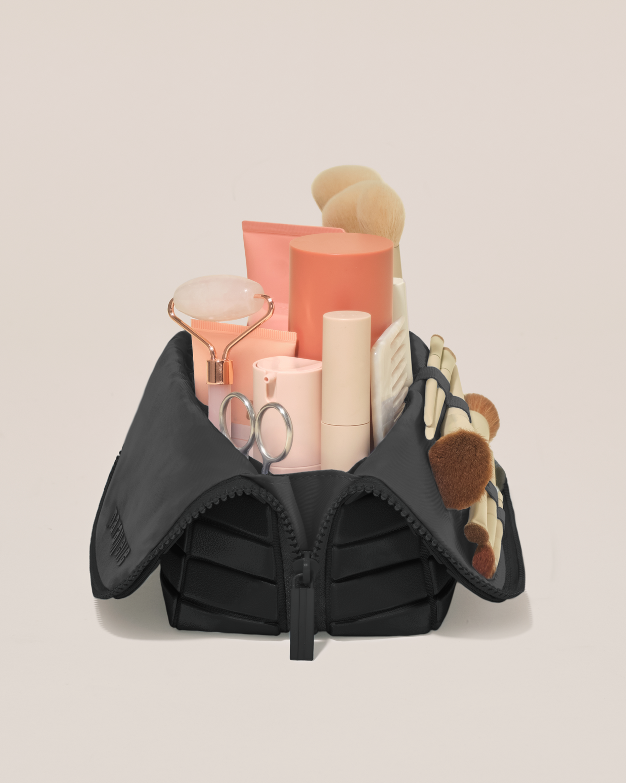 Side profile of the Medium Onyx (black) Traveller makeup bag filled with beauty essentials standing upright, showing flexible compartment design