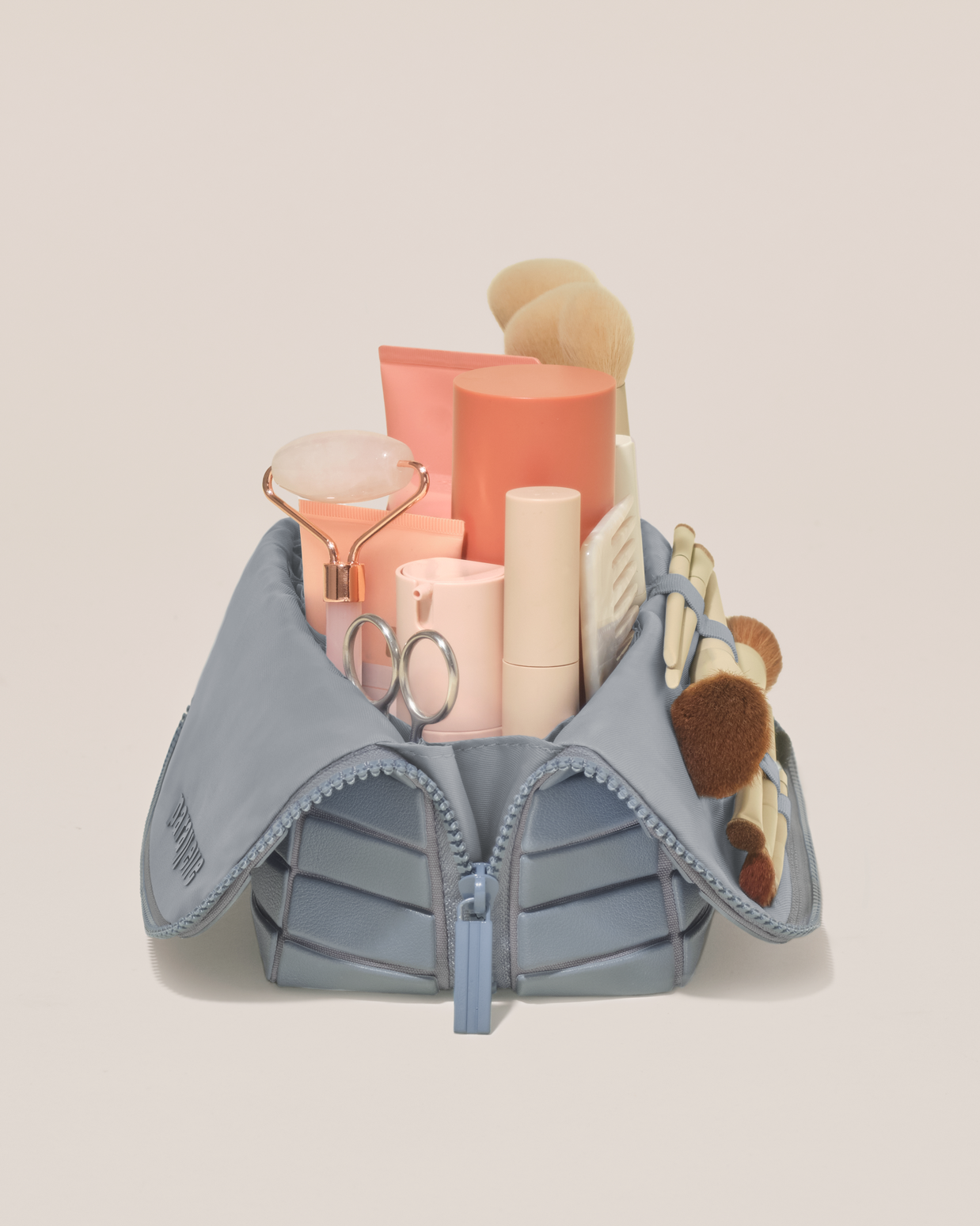 Side profile of the Medium Slate (blue) Traveller makeup bag filled with beauty essentials standing upright, showing flexible compartment design