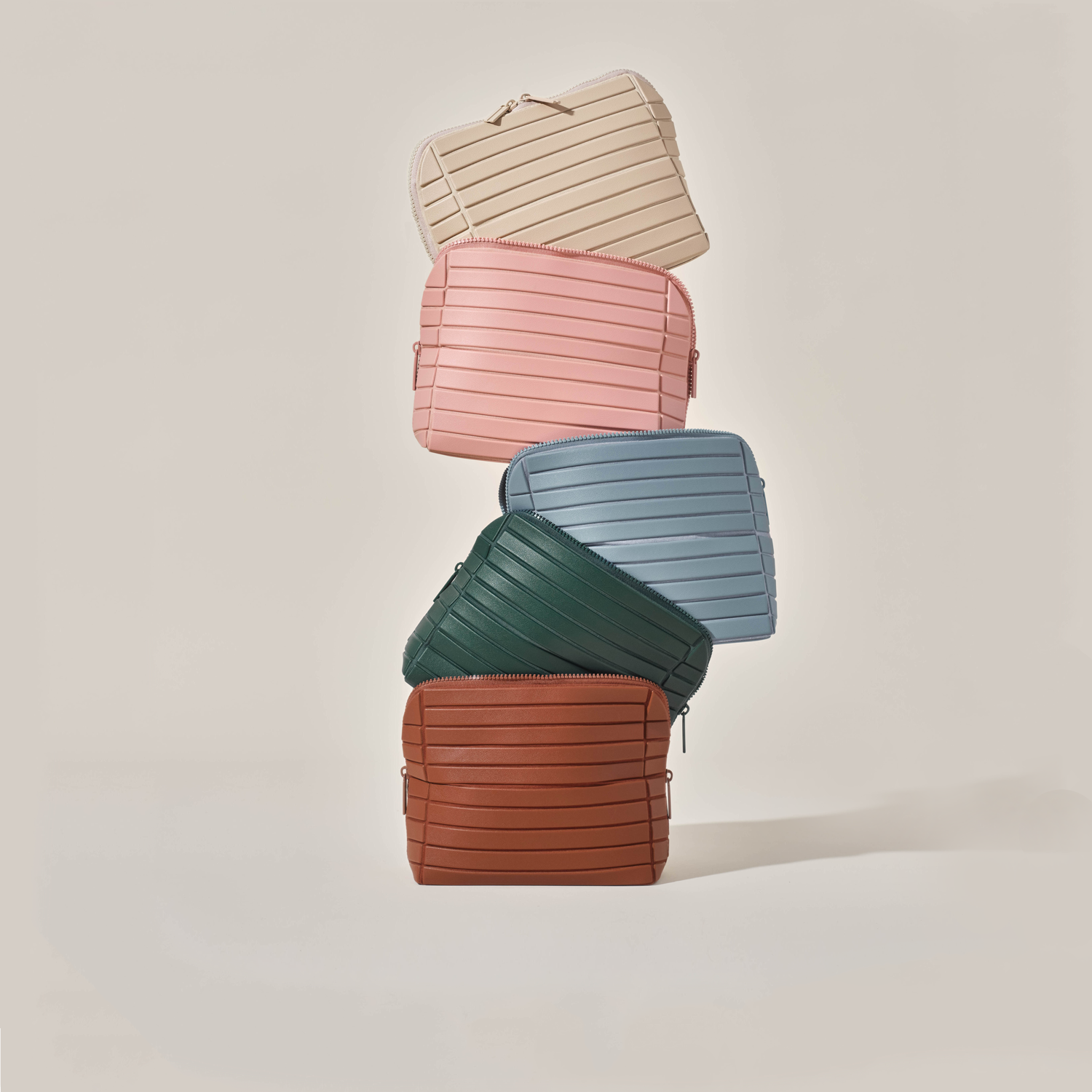 Medium Traveller makeup and toiletry organizer bags stacked in five colors: Bisque, Blush, Slate, Spruce, and Vicuna.