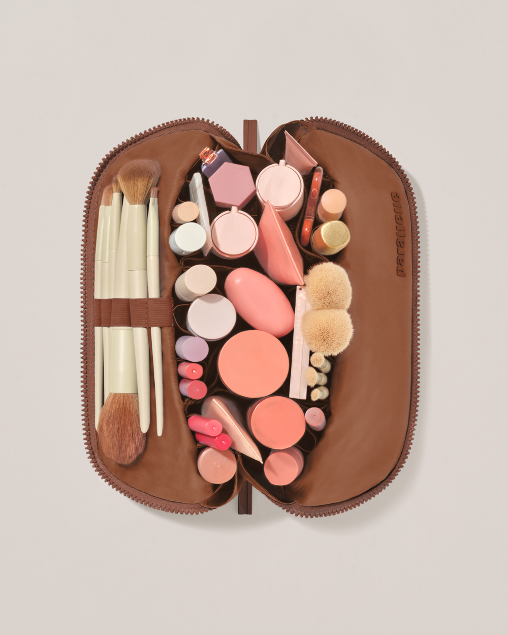 Overhead view of the Medium Vicuna (brown) Traveller makeup bag fully packed with upright beauty products and organized compartments