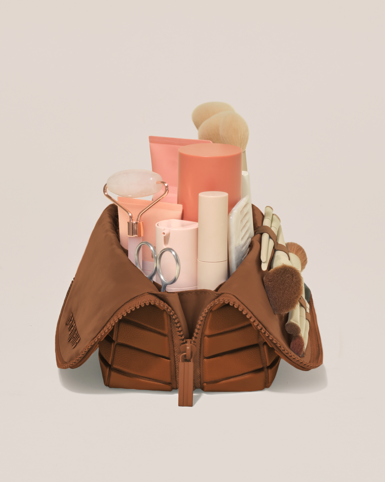 Side profile of the Medium Vicuna (brown) Traveller makeup bag filled with beauty essentials standing upright, showing flexible compartment design