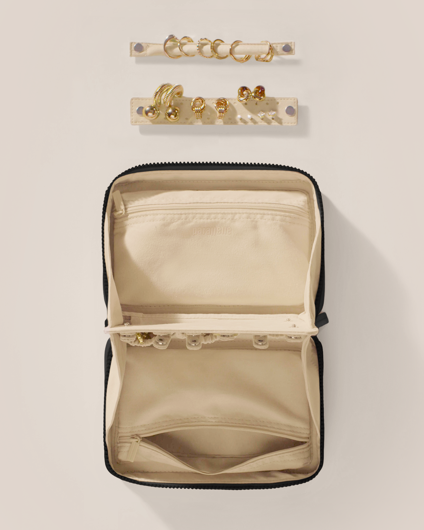 Overhead view of the Parallelle Onyx (Black) Vault, showcasing its two-sided interior with one side for rings and earrings and the other for necklaces. Both sides have a zipper pocket for watches and bracelets. The ring and earring bars' removable feature is shown