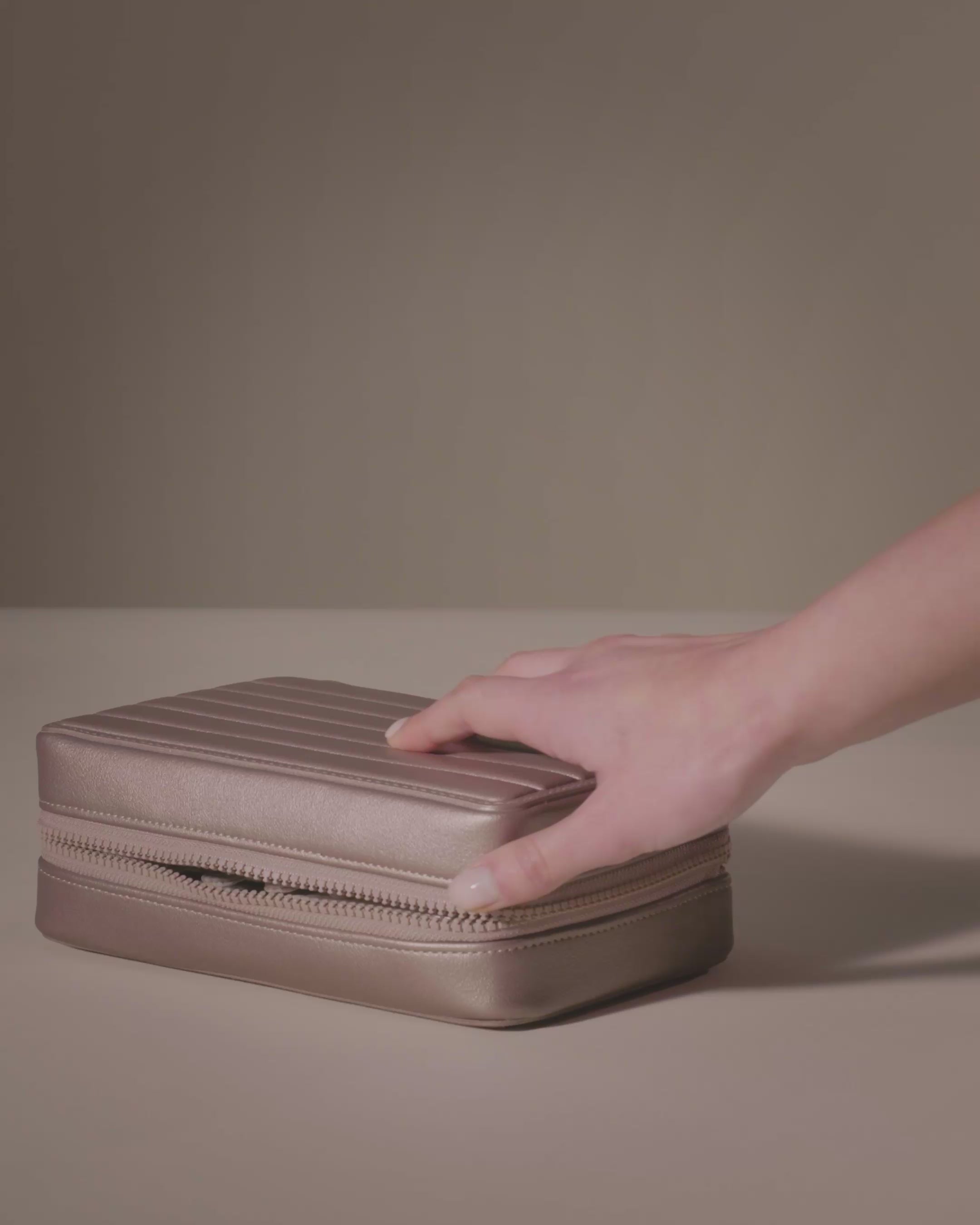 Parallelle Bronze Vault shown with two-sided interior with one side for rings and earrings and the other for necklaces. The ring and earring bars are shown being removed. Jewelry is shown being packed and organized on the ring bar, earring bar, necklace pouches, and zipper pouches.